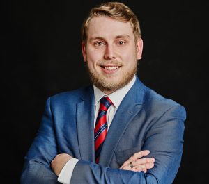 Jake Morgan, Head of Logistics and Supply Chain Services at Braddock Group, smiling and wearing a business suit, standing in an office environment.